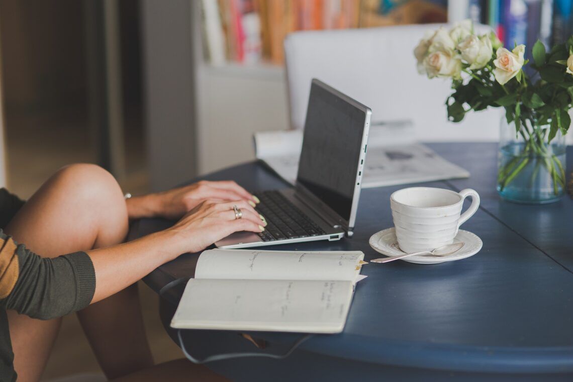 Mujer escribiendo con ordenador, taza de café y libro